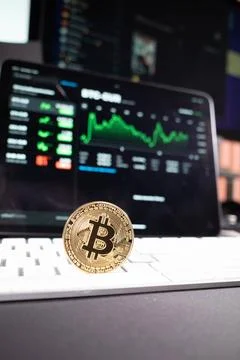 A bitcoin coin is standing on a computer keyboard and in the background is... Stock Photos