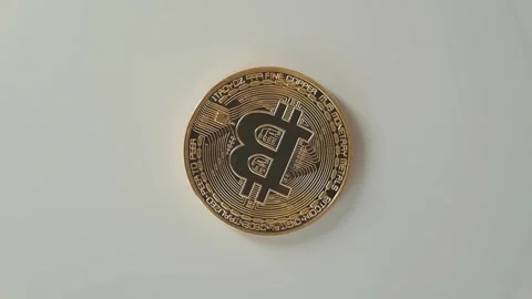 A Bitcoin coin is viewed from multiple angles on a plain surface in a studio Видео 338297742