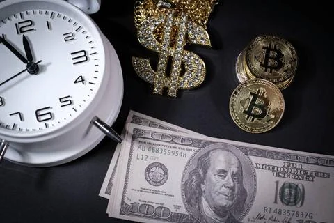 Bitcoin coins lie next to a stack of $100 bills, a white alarm clock and a... Stockfoto's