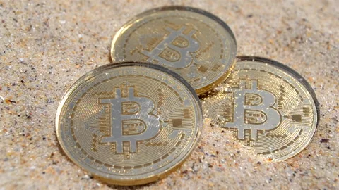 Bitcoin coins sand close up Three Bitcoin coins sprinkled with sand on sunny day Stock Footage 306164044