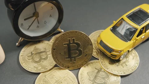 Bitcoin crypto coin on a grey board with yellow car, watch and wooden figures Stock-Footage 264074341
