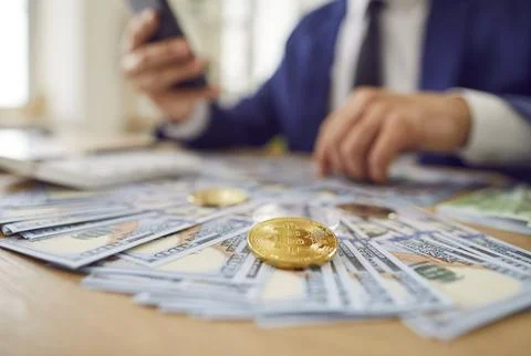 Bitcoin Gold Coin Resting On Stack Of Cash As Businessman Works With Phone Foto stock