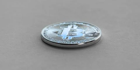 Bitcoin laying on flat surface. White metal coin. Stock Photos