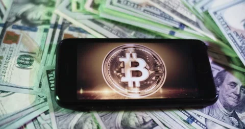 Bitcoin Logo on iphone surrounded by $100 Bills. Bitcoin Profits Layout. Stock Footage 169007991