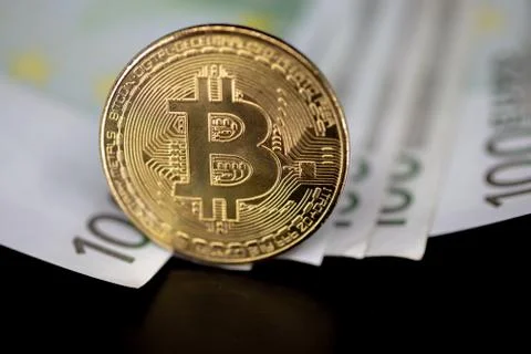Bitcoin token on black with reflection, on top of 100 euro banknotes money.  Stock-Fotos
