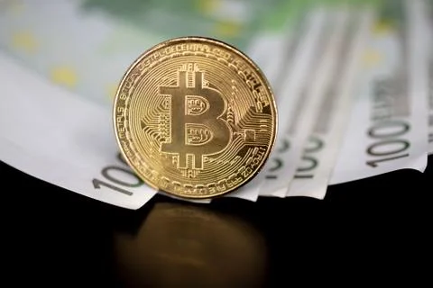 Bitcoin token on black with reflection, on top of 100 euro banknotes money.  Stock Photos