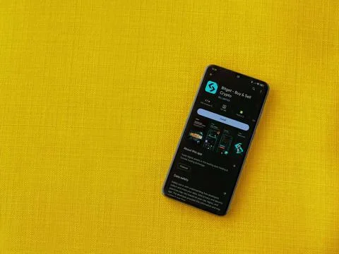 Bitget app play store page on smartphone on a yellow fabric background Stock Photos