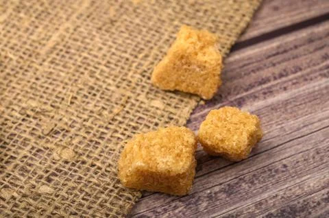 Bits of brown sugar and coarse homespun cloth on a wooden background. Close u Stock Photos
