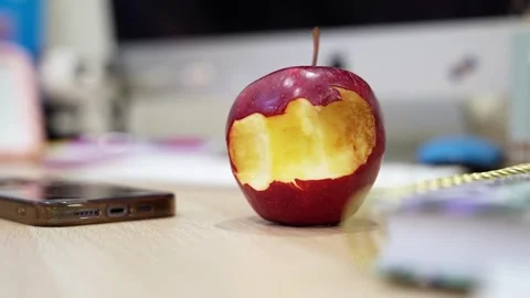 Bitten apple on desk with mobile phone and office supplies in background. Stock Footage 337748080