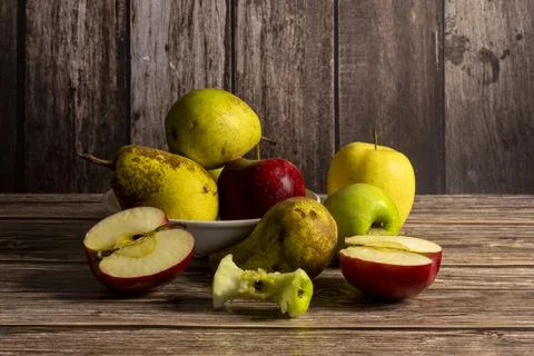 Bitten apples and pears in a ceramic bowl and scattered on an old wooden table Stock Photos