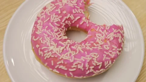 Bitten pink doughnut with sprinkles / rotating doughnut on a white plate Stock Footage 222922717