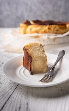 Bitten portion of basque burnt cheesecake on white plate with fork Stock Photos