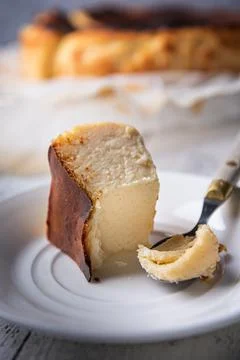 Bitten portion of basque burnt cheesecake on white plate with vintage spoon Stock Photos
