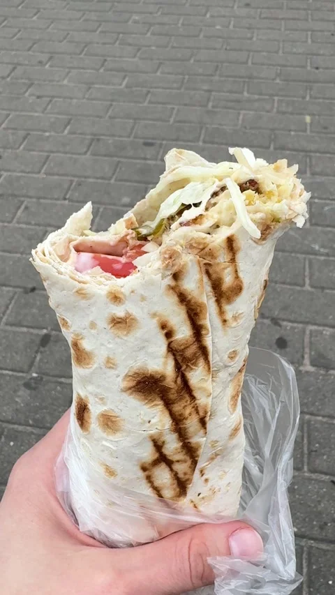 Bitten shawarma wrap in grilled lavash held by hand on urban street Vidéo 336542424