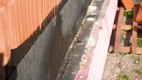 Bitumen waterproofing applied to foundation base along red brick wall exterior Stock Footage 310997588