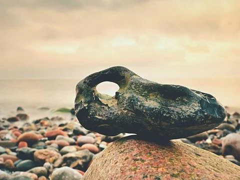 Bizzare rock on the pebbles beach, dramatic sky above. Stony offshore. Biz... Stock Photos
