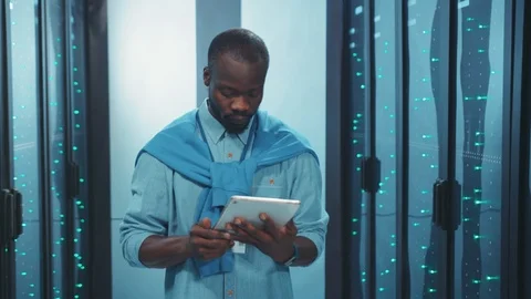 Black administrator using tablet checking servers hardware with digital laptop Stock Footage 119783018