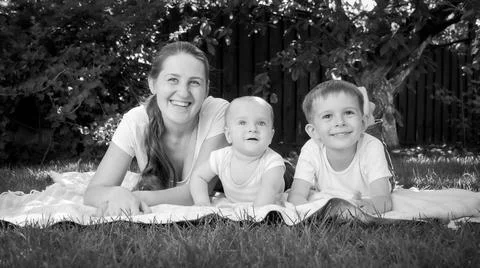 Black adn white portrait fo smiling boys lying with young mother on grass at Stock Photos