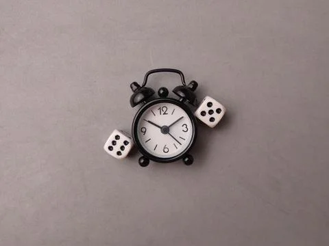 A black alarm clock is placed between two white dice showing different numb.. Stock Photos