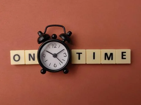A black alarm clock is positioned between letter tiles spelling ON TIME on .. Stock Photos