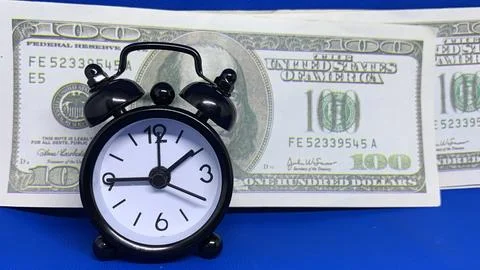 Black alarm clock positioned before a one-hundred-dollar bill, Stock Photos
