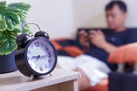 A black alarm clock sits on a table and a person playing game smartphone in.. Foto stock
