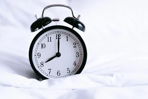 Black alarm clock on white bed. Time and hours concept. Interior and object.. Stock Photos
