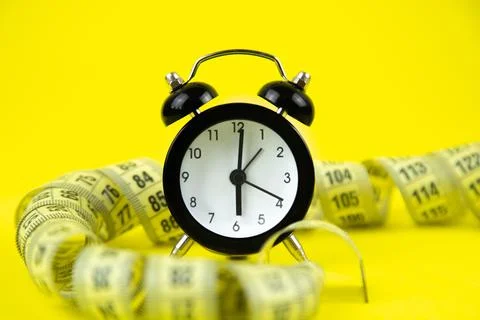 A black alarm clock with a white dial stands on a bright yellow background Stock Photos