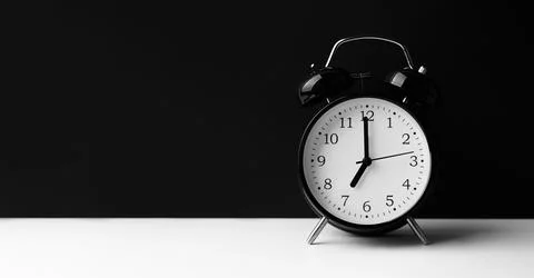 Black alarm clock on white table on black background. Stock Photos