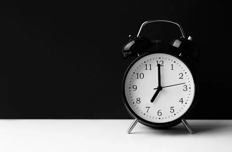 Black alarm clock on white table on black background. Stock Photos