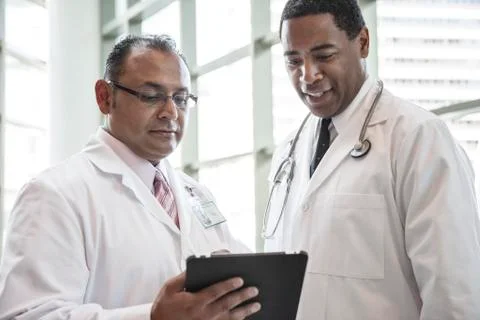 Black and Hispanic male doctors discussing a case in a hospital hallway. Stock Photos