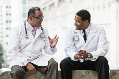Black and Hispanic male doctors discussing a case in a hospital hallway. Stock Photos