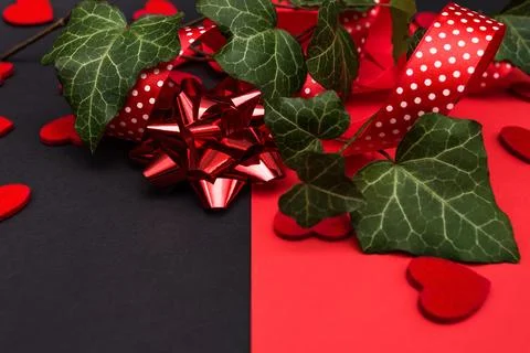 Black and red background with a red ribbon, a sprig of ivy and hearts Stock Photos