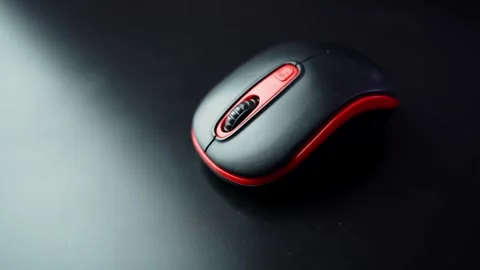 Black and red wireless computer mouse on a dark desk with soft studio light 스톡 동영상 331323103