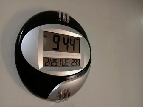 Black and silver round digital clock displaying time on wall. Stock Photos