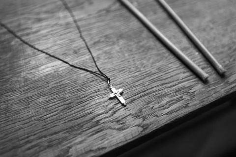 Black and white close up of a small silver cross necklace on a dark string Stock Photos