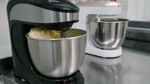 The black and white electric beaters are mixing the dough in steel pots on the Stock Footage 86423448