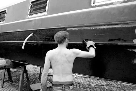 Black and white image of man painting boat. Stock Photos