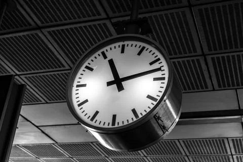 A black-and-white image of a round clock on a train station ceiling, showcasi Stock-Fotos