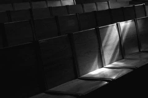Black and white image of rows of church pews with stream of light Stock Photos