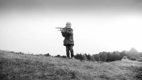 Black and white image of smiling little boy standing on hill top and throwing Stock Photos