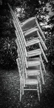 Black and white image of vertical stacked chairs outdoors. Stock Photos
