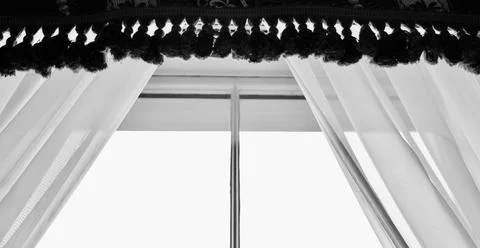 Black and white image of window dressed in voile and fringed pelmet Stock Photos