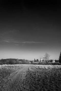 Black and white landscape of an empty field overlooking a distant church under a Stock Photos