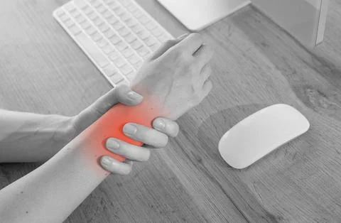 Black and white macro view of hand massaging aching wrist with red indicator. Stock Photos