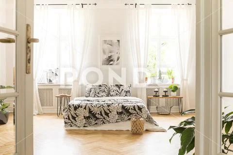 Black and white poster above bed with patterned pillows in bright spacious be Stock Photos