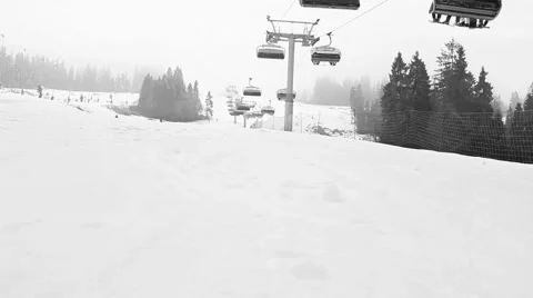 Black and white time lapse footage of ski lift transporting skiers up the hill Stock Footage