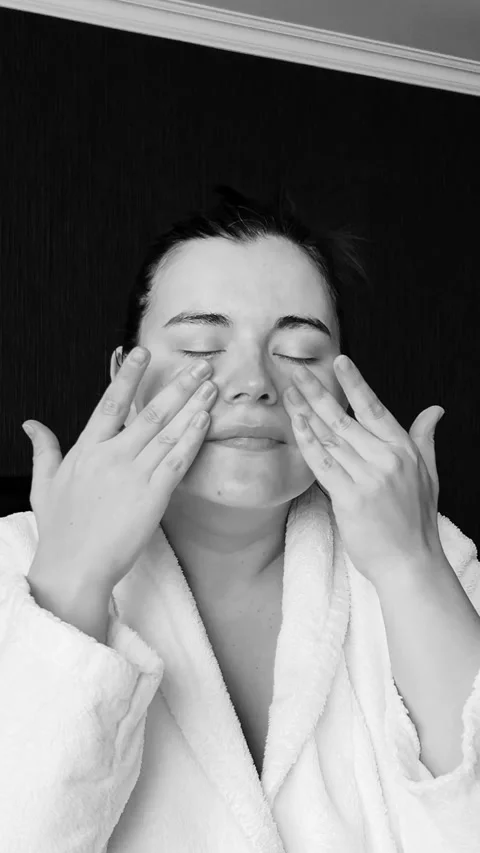 Black and white vertical 4K video. Woman in bath robe applies cream to face Stock Footage 269741137