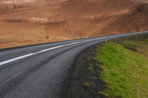 Black asphalt road separates dead land from fresh grass, Iceland Stock Photos