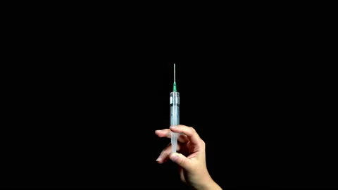 On a black background, a hand holds a syringe and squeezes out liquid from it Stock Footage 139715004